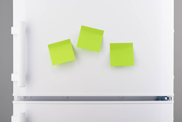 Three blank green sticky paper notes on white refrigerator  - Foto, Bild