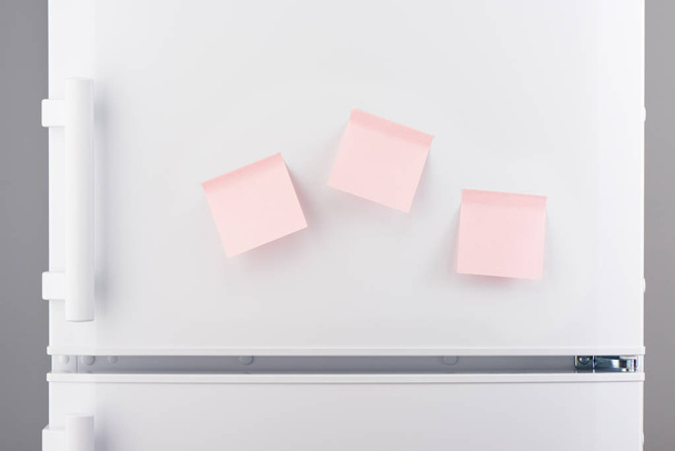 Three blank light pink sticky paper notes on white refrigerator - 写真・画像