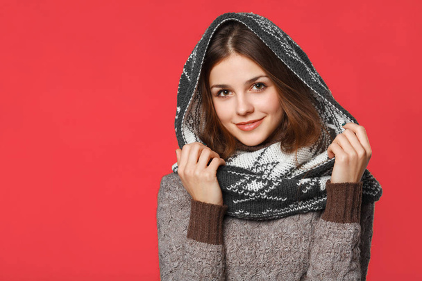 Kerst meisje dragen gebreide dragen sjaal. Mooie lachende meisje, winter concept, geïsoleerd op rode achtergrond - Foto, afbeelding