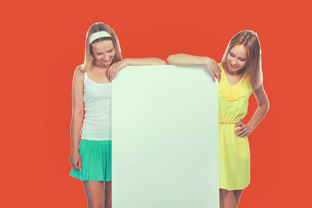 Portrait of a casual two young women standing near blank card - over white background - Photo, image