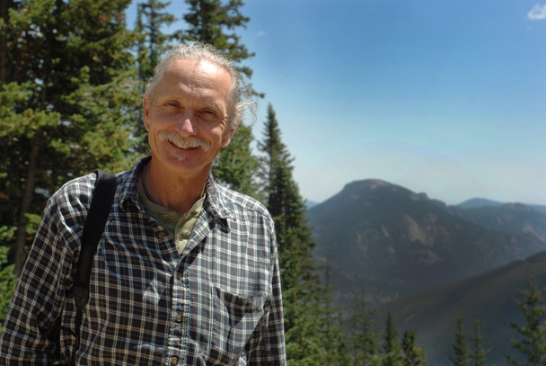 Sorrindo homem de meia idade perto de árvores, montanhas
 - Foto, Imagem