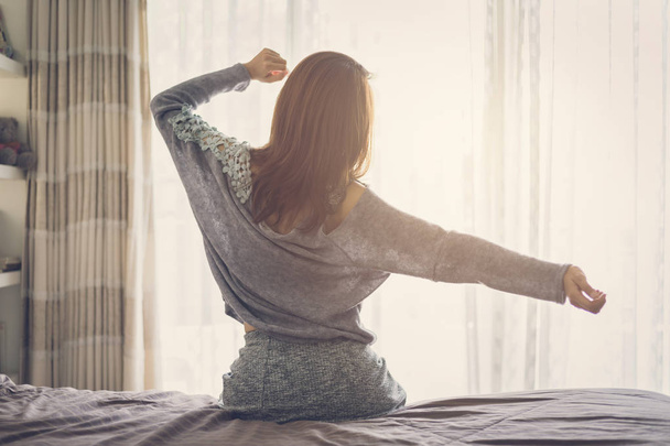 Woman stretching arms and waking up sitting on the bed - Valokuva, kuva