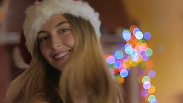 A beautiful young woman turns and looks at the camera wearing a santa hat - Filmati, video