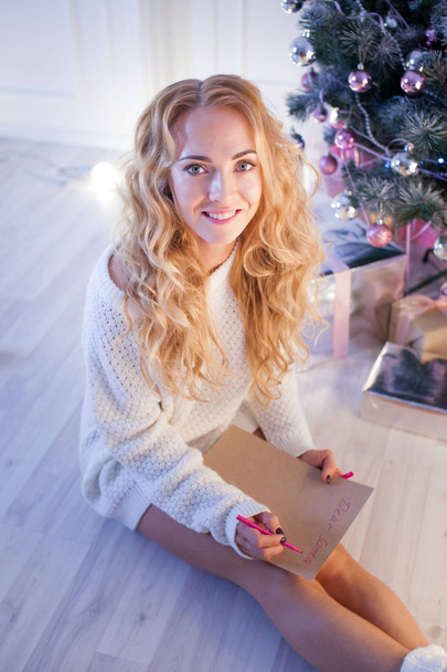 young pretty woman smiles and lying on carpet with a pen writing a christmas letter - Foto, Imagen