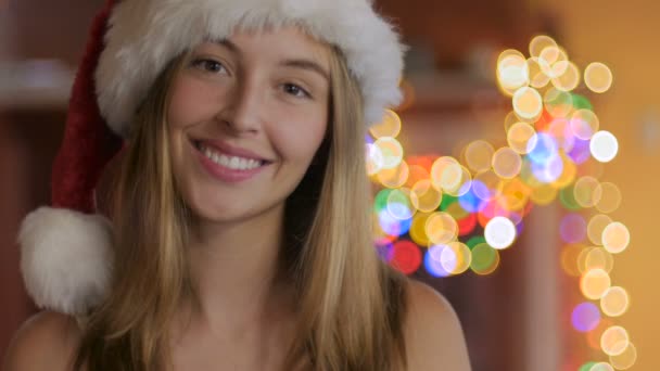 Beautiful blond woman smiles while wearing a Santa hat during Christmas - Video, Çekim