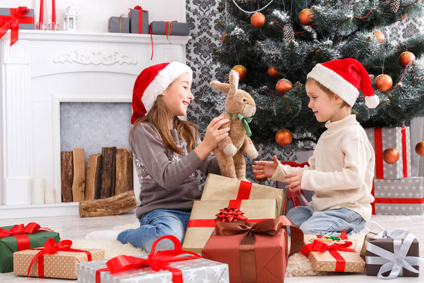Счастливые дети в шляпах Санты разворачивают рождественские подарки
 - Фото, изображение