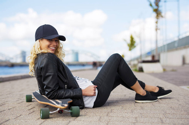 Woman with longboard sitting on the ground - Photo, Image