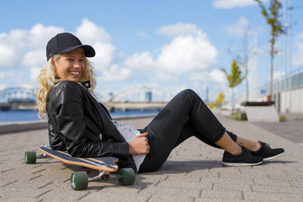Femme heureuse avec longboard assis sur le sol
 - Photo, image