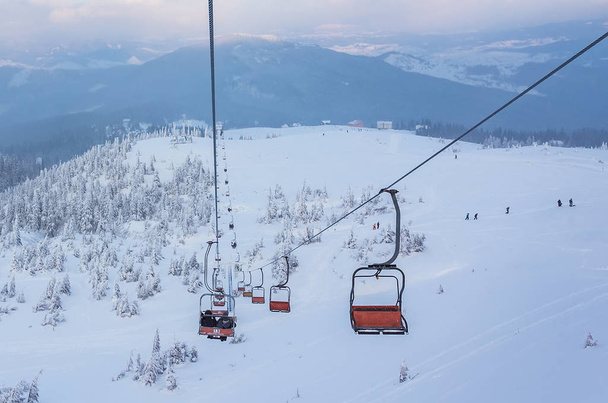 Elevador de esqui com assentos passando pela montanha e caminhos do céu
 - Foto, Imagem