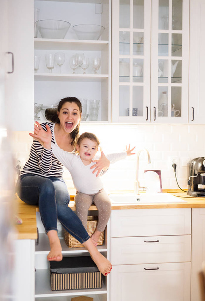 Mother with daughter in the kitchen sitting on countertop - Фото, зображення