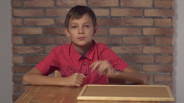 Kind sitzt am Schreibtisch mit Flipchart mit Schriftzug rufen Sie mich auf dem Hintergrund roten Backstein Wand - Filmmaterial, Video