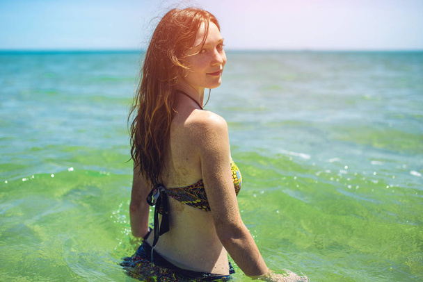 happy wet young woman standing back in blue sea - Photo, Image