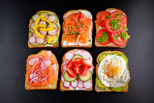 Varietà di panini vegetariani tostati con salmone, raddish, pomodori, cetriolo, avocado, uovo fritto e pepe dolce
 - Foto, immagini