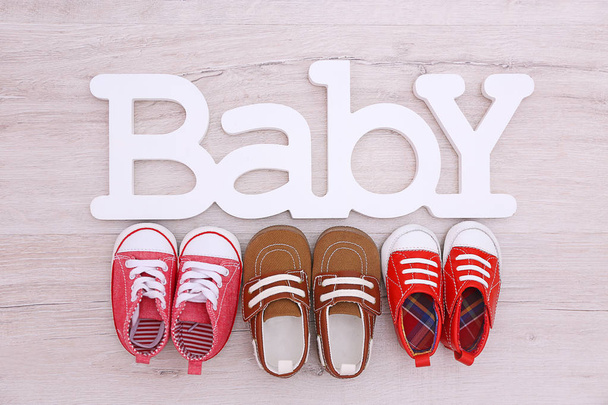 Different baby shoes and word BABY on wooden floor, top view - Fotografie, Obrázek