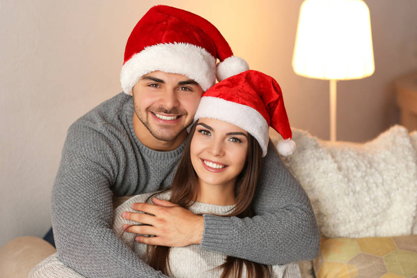 Young couple in Santa Claus hats resting at home - Photo, Image