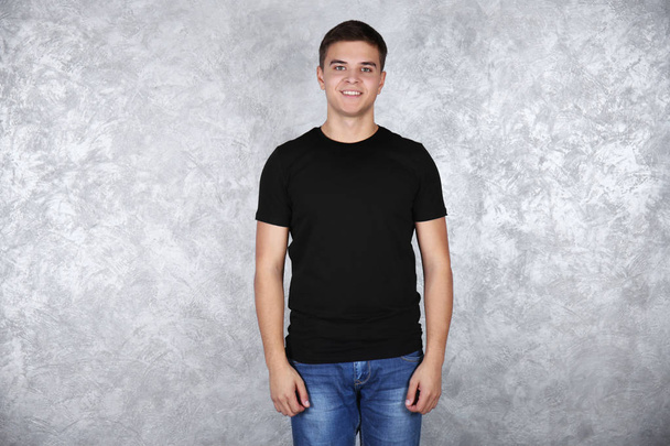 Yakışıklı genç gri dokulu duvar karşı boş siyah t-shirt ayakta - Fotoğraf, Görsel