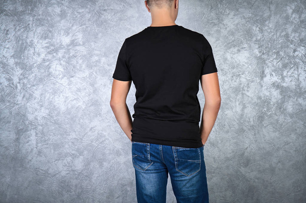 Handsome young man in blank black t-shirt standing against grey textured wall, close up - Foto, immagini