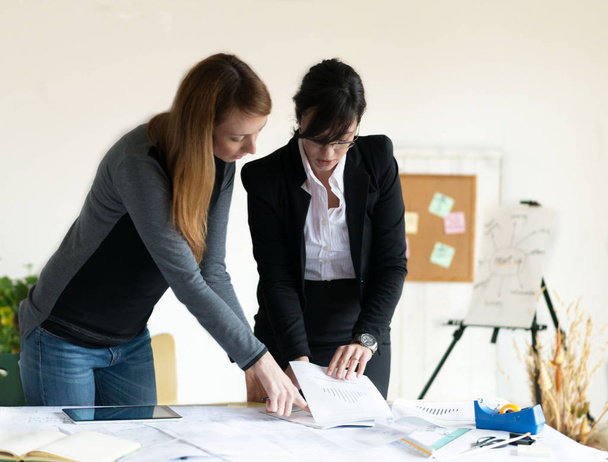 Jonge roodharige vrouwelijke architect en jonge vrouwelijke investeerder werken op kantoor.  - Foto, afbeelding