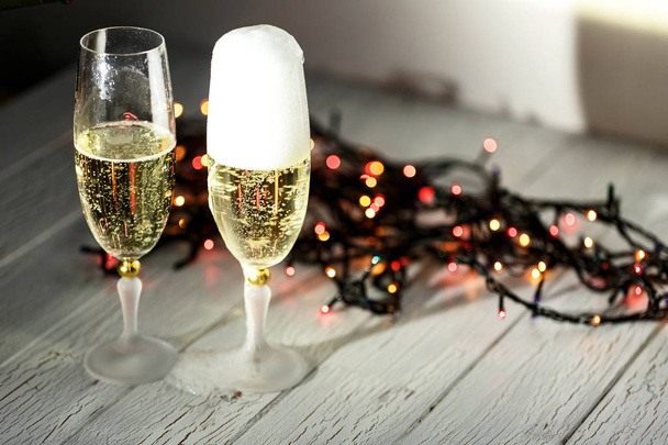 Two glasses of champagne and garland on a white floor - Фото, изображение