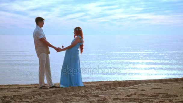 Pari pitää toisiaan kädestä meren rannalla auringonnousun aikaan. Raskaana pari ranta
 - Materiaali, video