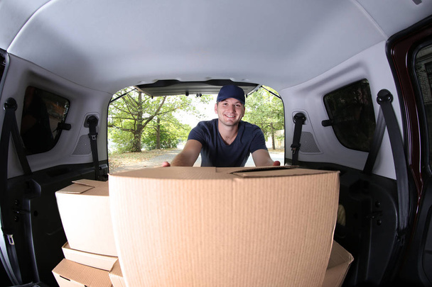 Jovem entregador masculino carregando caixas no carro
 - Foto, Imagem