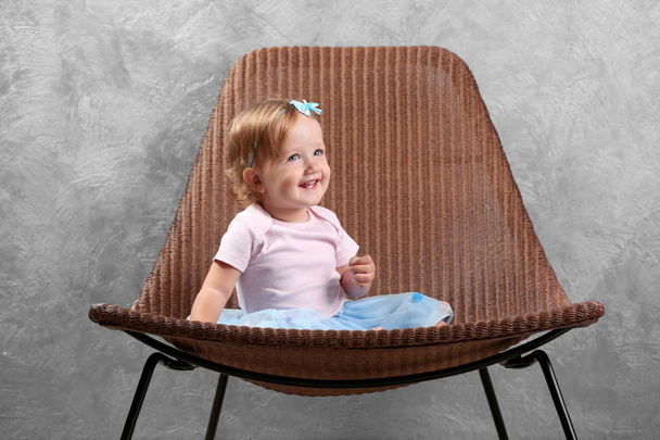 Little fashion-girl sitting on designer chair on gray wall background - Foto, imagen