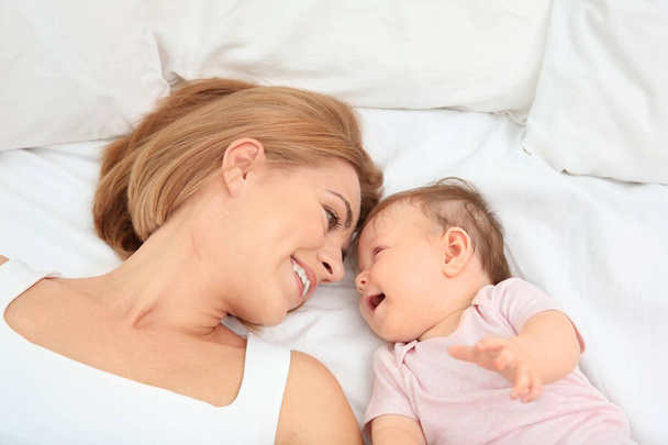 Young mother and baby lying on bed - 写真・画像