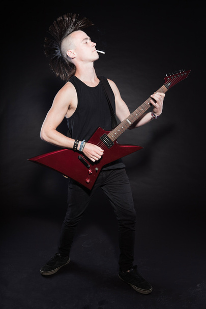 Punkrock-Mann mit roter E-Gitarre und Mohawk-Frisur. Gesichtsausdruck. isoliert auf schwarzem Hintergrund. Studioaufnahme. - Foto, Bild