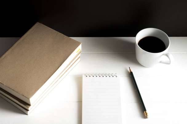 Posto di lavoro con blocco note, libro e tazza di caffè nero su tavolo in legno bianco
. - Foto, immagini
