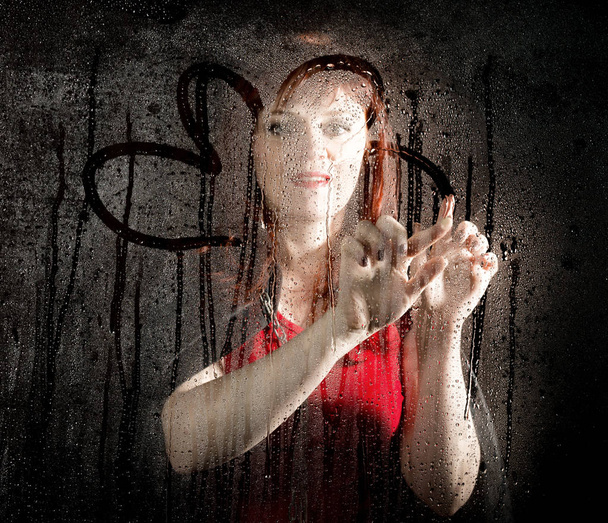 Smooth portrait of female model, posing behind transparent glass and painting on water drops. young smiling woman - Foto, afbeelding