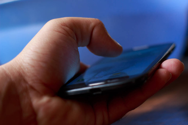 Close-up van jonge jongens hand met smartphone. Blauwe onscherpe achtergrond - Foto, afbeelding