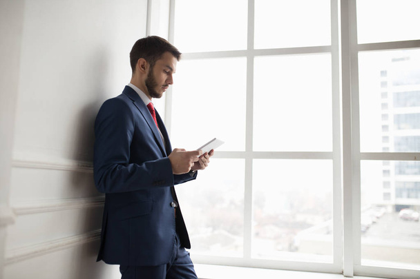 Businessman in white office using digital tablet at window - Foto, Imagem