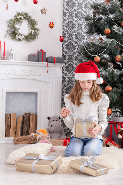 Красива дівчина в капелюсі Санта розгортає різдвяні подарунки
 - Фото, зображення