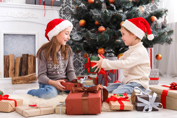 Crianças felizes em chapéus de Papai Noel desembrulhando presentes de Natal
 - Foto, Imagem