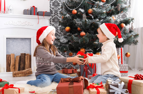 Niños felices en sombreros de Papá Noel desenvolviendo regalos de Navidad
 - Foto, imagen