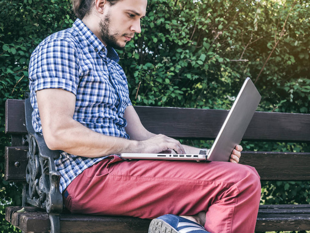 Young Man working on his laptop sitting on the bench in the park - Foto, immagini