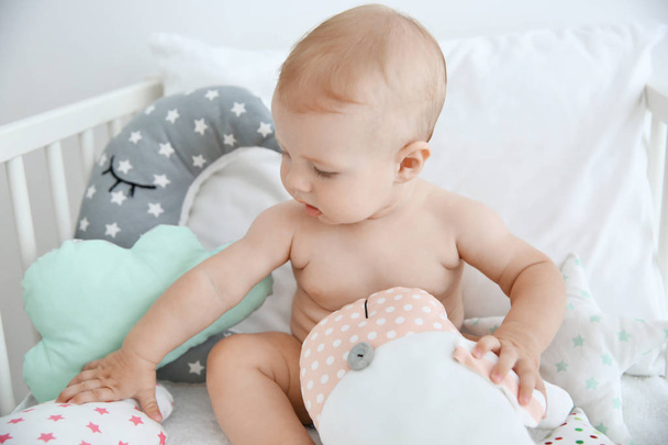 Cute little baby with pillows sitting in crib - 写真・画像