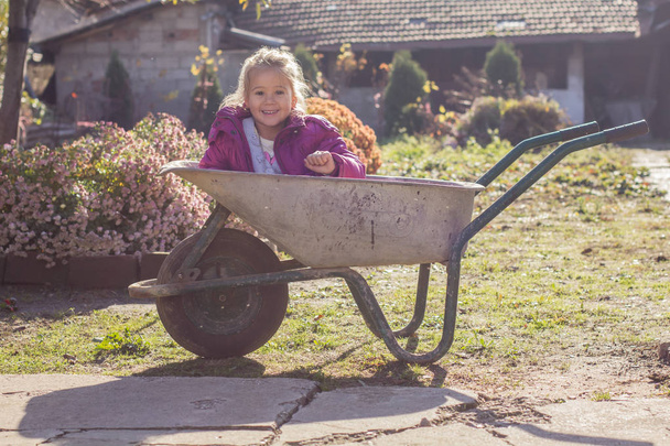 Happy little girl sitting in wheelbarrow - Фото, изображение