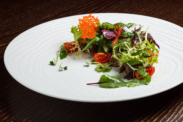 Gemüsesalatmenü für das Restaurant in einem großen weißen Teller auf einer weißen Tischdecke auf einem Holztisch. Salat mit Messer und Gabel auf den Tisch. svezhive Gemüse. - Foto, Bild