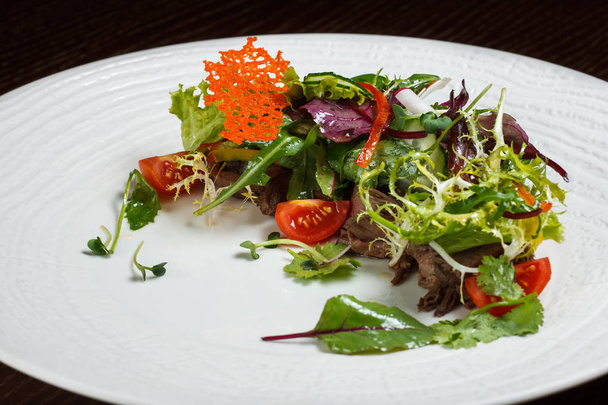 Gemüsesalatmenü für das Restaurant in einem großen weißen Teller auf einer weißen Tischdecke auf einem Holztisch. Salat mit Messer und Gabel auf den Tisch. svezhive Gemüse. - Foto, Bild