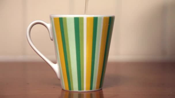 Enchendo uma xícara colorida com chá em pé na mesa de madeira na cozinha
. - Filmagem, Vídeo