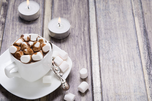 Hot chocolate with marshmallow in white cup and two candles on wooden table - Foto, Imagem