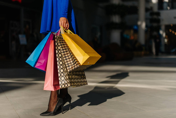 Beautiful legs of young pretty woman in short blue dress with long sleeves and shoes on hight heels after shopping in big mall. Many shopping bags in her hands. - Foto, afbeelding