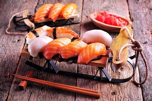 hausgemachtes Sushi mit Lachs, Tintenfisch und Garnelen auf kleinem Schlitten Weihnachten Hintergrund - Foto, Bild