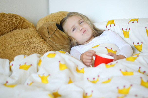 Kislány fogott, influenza, és iszik forró teát citrommal, az ágyban - Fotó, kép