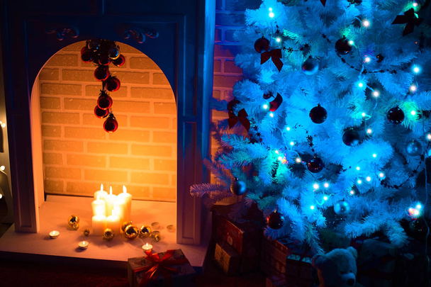 Kivilágított karácsonyfa mellett egy kandalló. Világos karácsonyi fények a sötétben. Új év Karácsony este. Karácsony estéjén. Belső elrendezése. - Fotó, kép