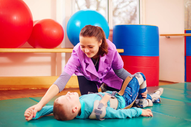cute kid with disability has musculoskeletal therapy by doing exercises in body fixing belts - Foto, Bild