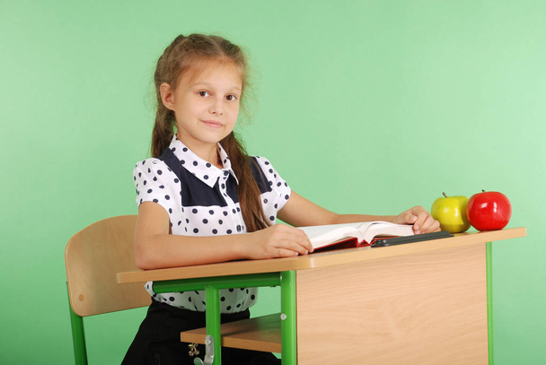 Girl in a school uniform sitting at a desk and reading a book - Photo, Image