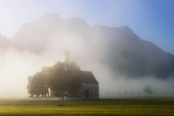 Chiesa di San Colomano con luce calda che brilla nella nebbia durante l'alba nei pressi del Castello di Neuschwanstein, Fussen, Baviera, Germania
 - Foto, immagini