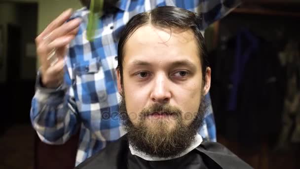 Barber making haircut of attractive bearded man in barbershop - Felvétel, videó